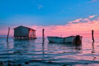 Deretan perahu kayu tradisional milik nelayan bersandar rapi di tepi permukiman panggung pesisir Indonesia saat senja menyapa.