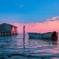 Deretan perahu kayu tradisional milik nelayan bersandar rapi di tepi permukiman panggung pesisir Indonesia saat senja menyapa.