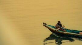 Seorang nelayan tradisional menyiap jaringan perahu kayunya di pesisir pantai Indonesia saat matahari terbenam. Kehidupan masyarakat pesisir tetap menyatu erat dengan ritme alam dan laut Nusantara.