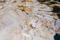 Pemandangan kawah bekas galian tambang terbuka yang mengubah lanskap hutan tropis hijau menjadi bentang tanah gersang dan genangan air asam beracun di pedalaman Indonesia.