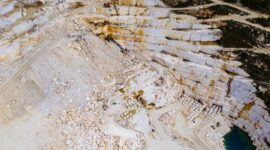 Pemandangan kawah bekas galian tambang terbuka yang mengubah lanskap hutan tropis hijau menjadi bentang tanah gersang dan genangan air asam beracun di pedalaman Indonesia.