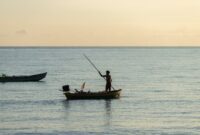 Seorang nelayan tradisional di pesisir Nusantara bersiap melaut menggunakan perahu kayu sembari memanfaatkan keindahan alam matahari terbenam. Aktivitas bahari masyarakat pesisir kini memadukan kearifan lokal dan inovasi ekonomi baru.