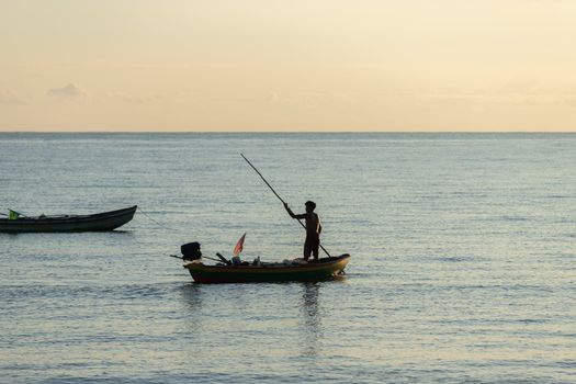 Seorang nelayan tradisional di pesisir Nusantara bersiap melaut menggunakan perahu kayu sembari memanfaatkan keindahan alam matahari terbenam. Aktivitas bahari masyarakat pesisir kini memadukan kearifan lokal dan inovasi ekonomi baru.