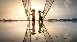 Deretan perahu kayu nelayan tradisional tertambat rapi di pinggir dermaga sebuah desa pesisir Indonesia saat matahari terbenam menyinari perairan pantai.