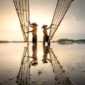 Deretan perahu kayu nelayan tradisional tertambat rapi di pinggir dermaga sebuah desa pesisir Indonesia saat matahari terbenam menyinari perairan pantai.
