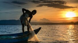 Seorang nelayan tradisional di atas perahu kayu bersiap melaut menyongsong matahari terbit, menggambarkan keharmonisan antara kehidupan masyarakat pesisir dan bentang alam bahari Nusantara.