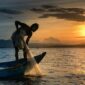 Seorang nelayan tradisional di atas perahu kayu bersiap melaut menyongsong matahari terbit, menggambarkan keharmonisan antara kehidupan masyarakat pesisir dan bentang alam bahari Nusantara.