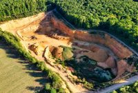 Lahan bekas penambangan terbuka di wilayah pedalaman Indonesia yang mengubah lanskap hutan hujan tropis menjadi galian tanah merah, mencerminkan harga ekologis yang harus dibayar demi pemenuhan komoditas mineral global.